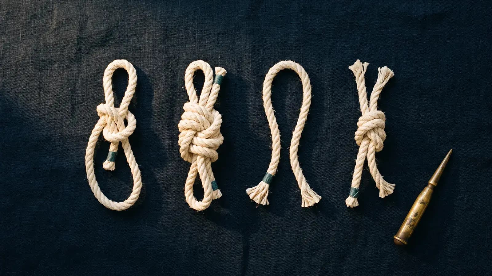Quatre cordages noués différemment alignés sur un lin bleu nuit, un épissoir de laiton posé à droite